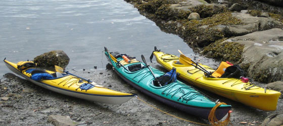 Three kayaks, paddles, and life vests waiting on rocky shore